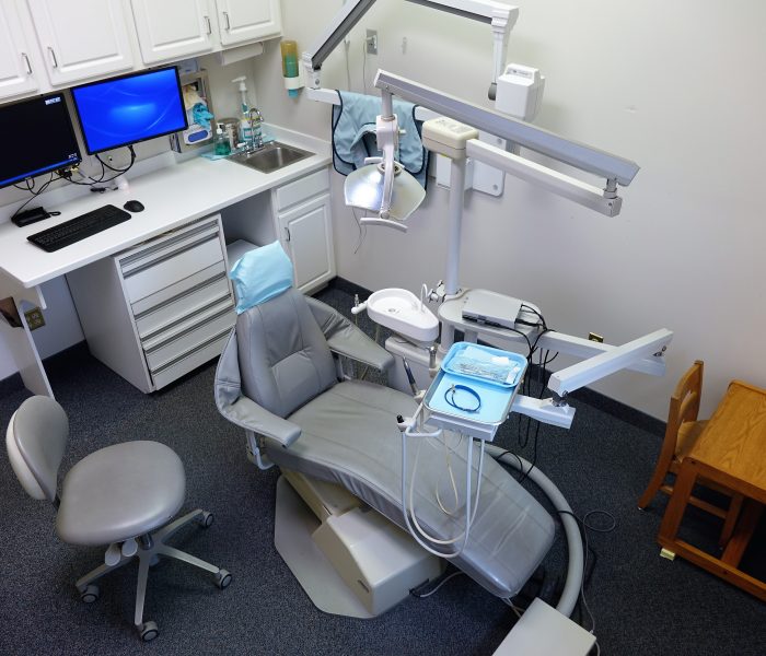 dental chair and desk with a computer on it inside of a dental exam room