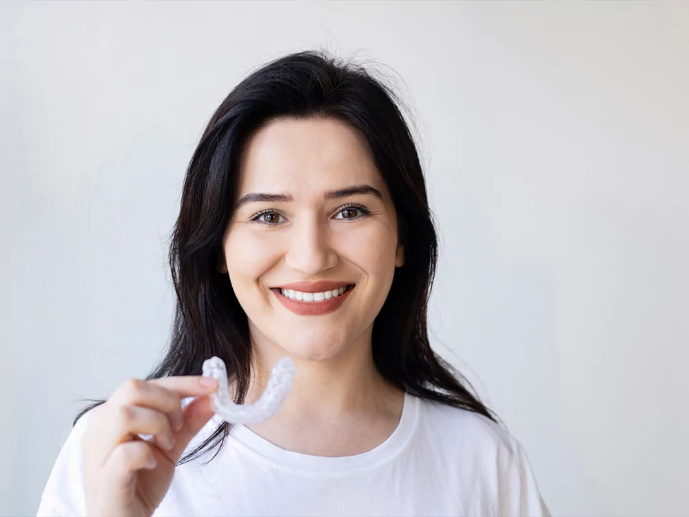 Woman smiling holding Invisalign clear aligner