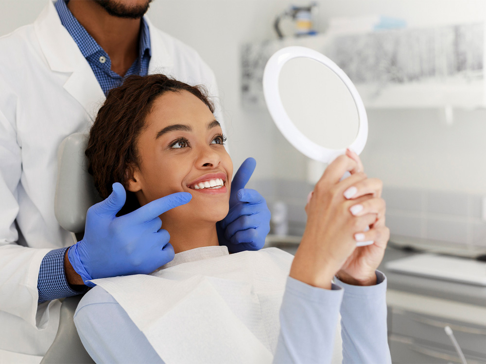 doctor pointing to a patient's teeth while she smiles into a mirror